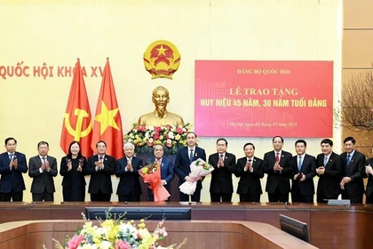 El presidente de la Asamblea Nacional, Tran Thanh Man, y funcionarios felicitan a Duong Thanh Binh y Phung Khanh Tai (con flores) por la concesión de las insignias de 45 y 30 años de membresía del Partido. (Foto: nhandan.vn)